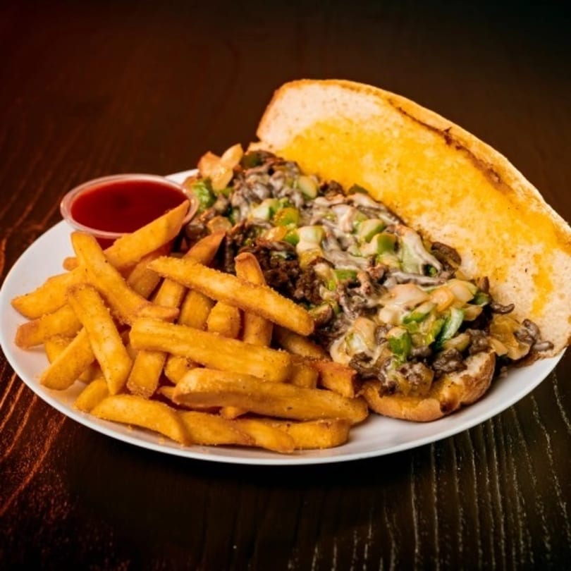 Deens Cheesesteak and Pizza's cheesesteak sandwich with fries and ketchup on a white plate.
